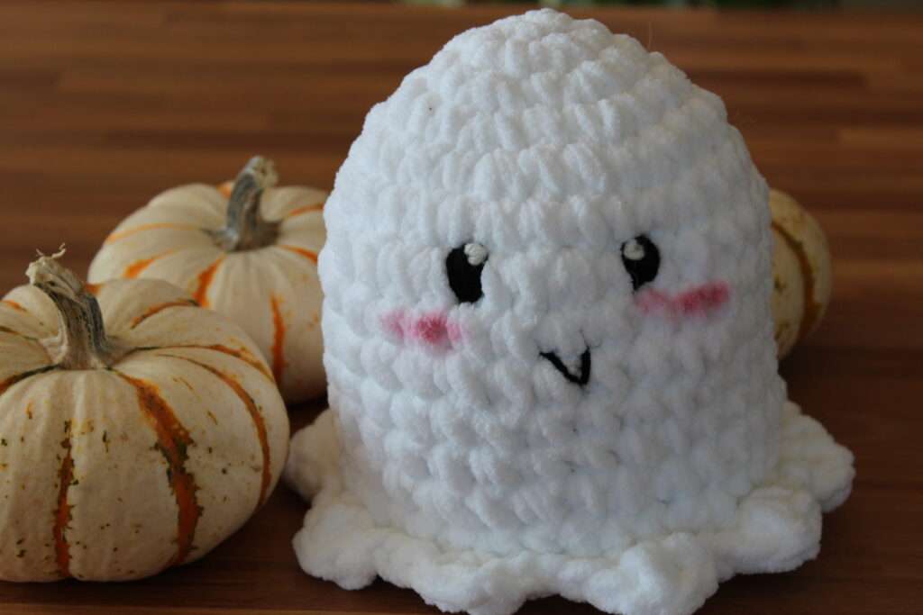 close up of a crochet ghost amigurumi plushie with pumpkins in the background