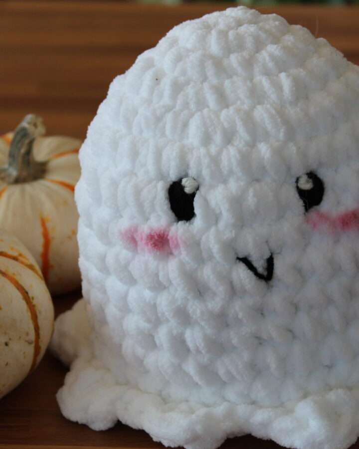 close up of a crochet ghost amigurumi plushie with pumpkins in the background